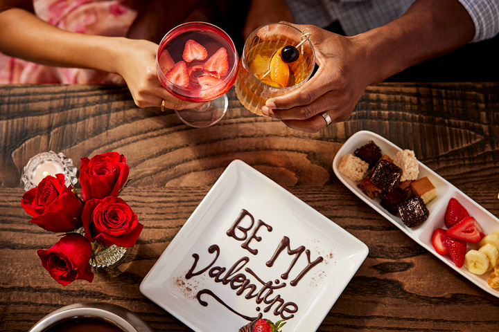 a couple holding drinks and a plate of desserts