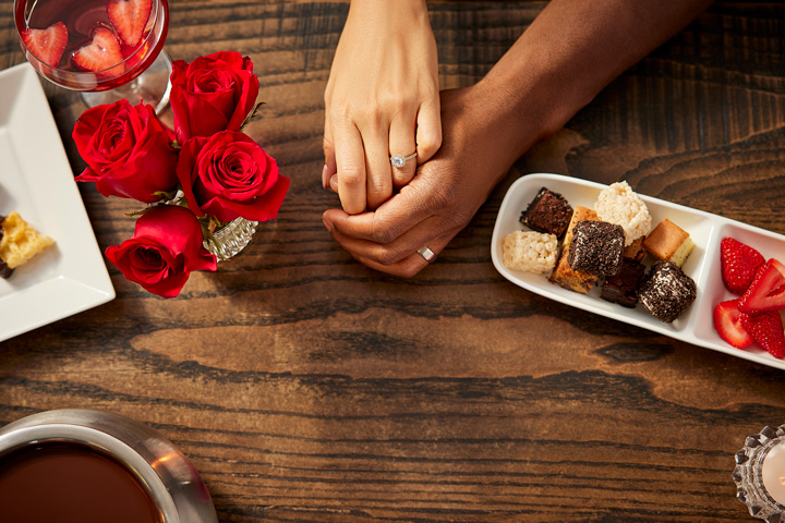 a couple holding hands next to a plate of desserts and a glass of wine