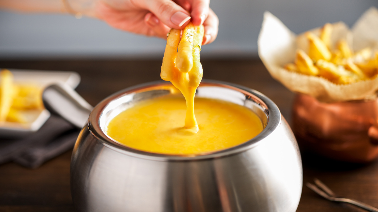 Person dipping Melting Pot Rosemary Fries in cheese fondue