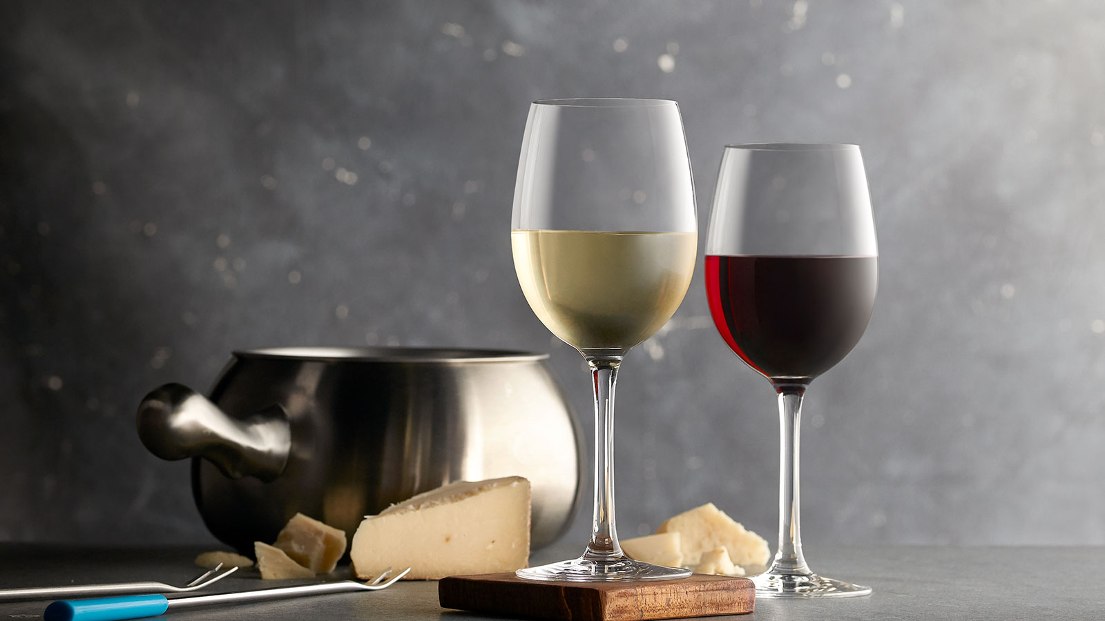 a couple of wine glasses next to a pot of cheese