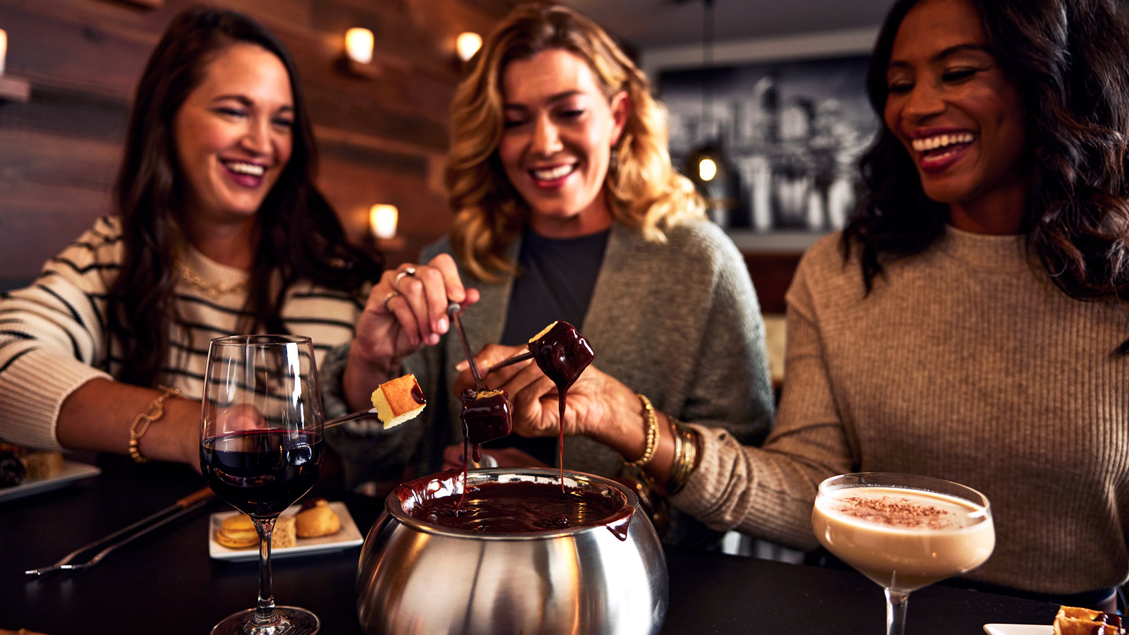 a group of women smiling and dipping chocolate into a fondue pot